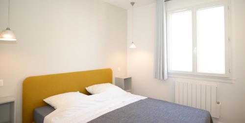 1 dormitorio con 1 cama con cabecero amarillo y ventana en Appart' Préférence, en Lyon