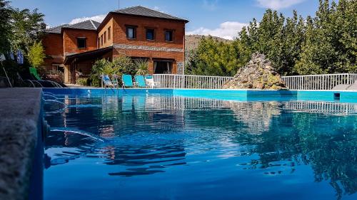 una piscina de agua azul frente a una casa en Hotel Rural Don Burguillo, en El Tiemblo
