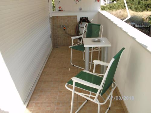 a small porch with two green chairs and a table at Nina Rooms (apartments) in Artemida