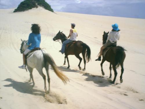three people riding horses on the beach at Hotel Enseada Maracajaú in Maracajaú