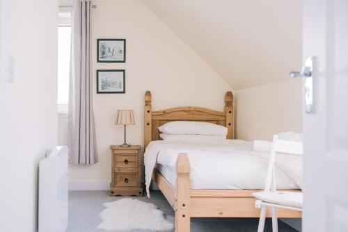 a white bedroom with a wooden bed and a chair at Sea Shimmer in Portree