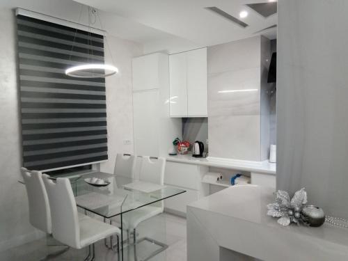 a white kitchen with a glass table and white chairs at N&L in Banja Luka
