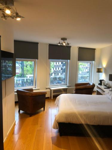 a bedroom with a bed and two chairs and windows at Bridge Inn in Amsterdam
