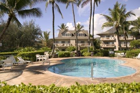 a swimming pool in front of a house with palm trees at CASTLE Kaha Lani Resort in Kapaa