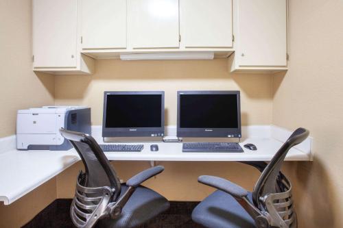 a desk with a computer and two monitors and two chairs at Baymont by Wyndham Saraland in Saraland