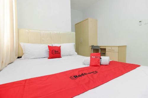 a large white bed with a red blanket on it at RedDoorz near Siloam Hospital Palembang in Palembang
