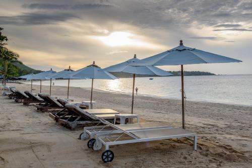 a row of beach umbrellas and tables on a beach at Samui Jasmine Resort - SHA Plus in Lamai