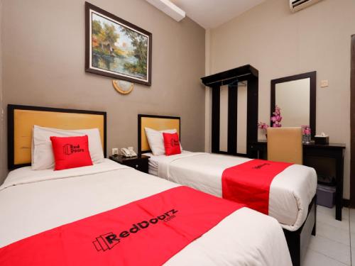 two beds in a hotel room with red and white sheets at RedDoorz Plus @ Singosari Raya in Semarang