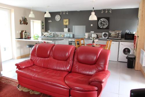 a red leather couch in a living room with a kitchen at Cute Gite family Aucey Mont Saint Michel in Aucey-la-Plaine