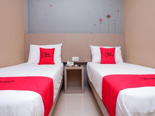 RedDoorz near Java Supermall Semarang في سيمارانغ: سريرين في غرفة الفندق مع وسائد حمراء