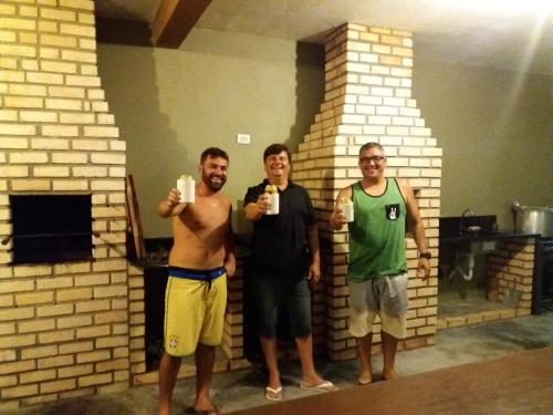 three men are standing in front of a brick fireplace at Vila Alegria in Bombinhas