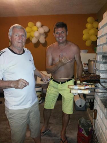 a shirtless man standing next to a man cutting a cake at Vila Alegria in Bombinhas
