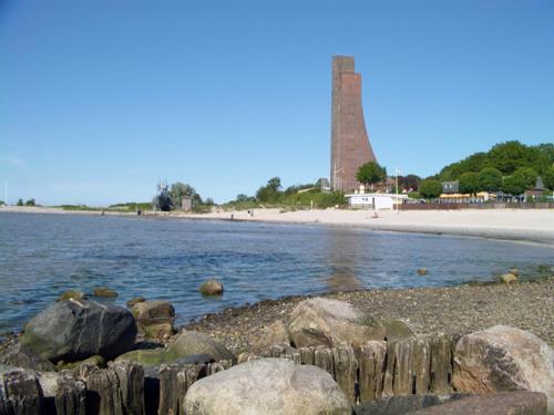 a beach with rocks and a lighthouse in the background at Hotel Admiral Scheer in Laboe