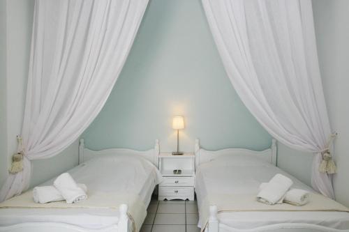 two beds in a room with white curtains at Studios Eleni I in Tinos