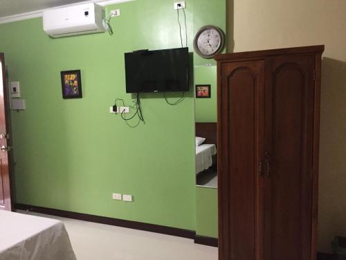 een kamer met een groene muur met een klok en een tv bij Golden Pension House,Palawan in Puerto Princesa City