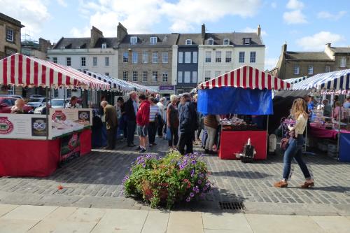 a group of people walking through a market with red and white tents at Abbey View in Kelso