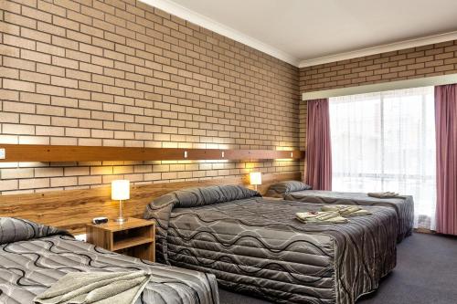 a hotel room with two beds and a brick wall at Holbrook Town Centre Motor Inn in Holbrook