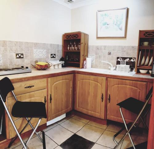 - une cuisine avec des placards en bois, un évier et 2 chaises dans l'établissement The Old Chapel Cottage, à Leighton Buzzard