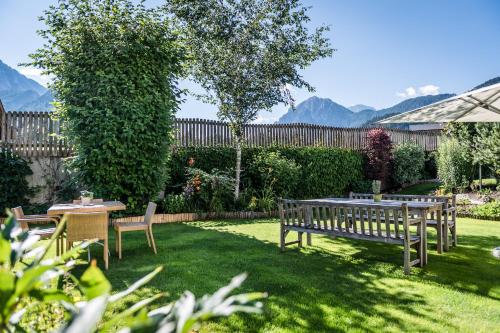 a garden with two wooden benches and a table at Sporthotel Exclusive in San Vigilio Di Marebbe