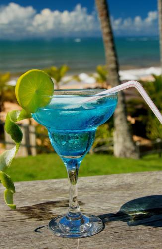 a blue drink in a glass on a table with the beach at Rio Da Barra Villa Hotel in Trancoso