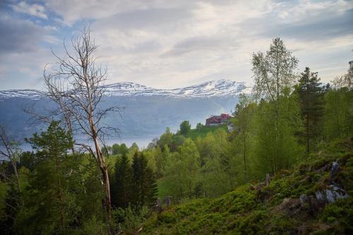 a snow covered mountain in the distance with a house on a hill at Panorama view along the fjord in Stryn in Blakset