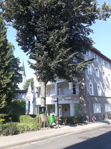 a large white building with a tree in front of it at Apartament pod Zakrytym Mostem in Lądek-Zdrój