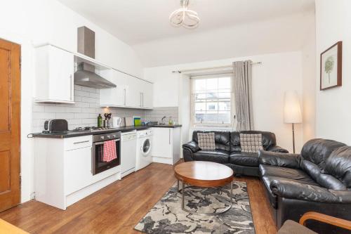 a living room with a black leather couch and a kitchen at Old Town Edinburgh Apartment close to Castle and Royal Mile in Edinburgh