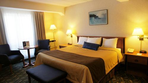 a hotel room with a bed and two chairs at Travelodge by Wyndham Niagara Falls At the Falls in Niagara Falls