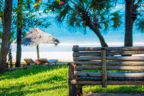 a wooden bench in front of a beach with an umbrella at Amani Beach Resort in Kutani