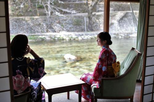 Kagamino的住宿－OkutsuHotSpa IkedayaKajikaen，两个和服女装坐在窗边