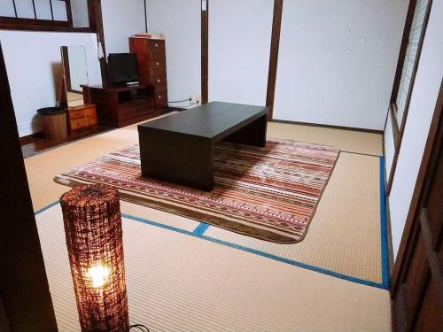 a room with a table on a rug and a lamp at Yufuin Country Road Youth Hostel in Yufuin