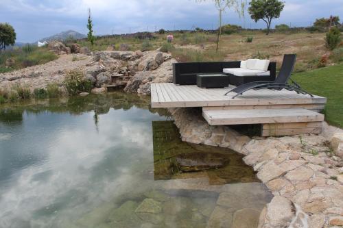 a bench and chair sitting on a deck over a body of water at Finca el enebro in Valdemorillo