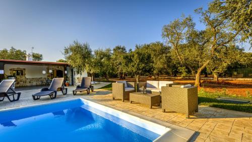 a swimming pool with chairs and a yard with trees at Trullo degli Augelli in San Michele Salentino