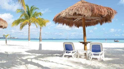 two chairs and a table and umbrella on a beach at Cancun Beachfront Condo in Cancún