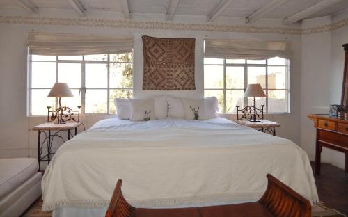 a bedroom with a large white bed with two windows at Suites Santo Domingo in San Miguel de Allende