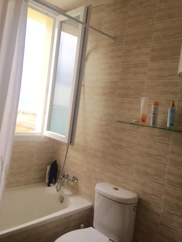 a bathroom with a toilet and a window and a tub at Apartamentos vista a tres continentes in La Línea de la Concepción