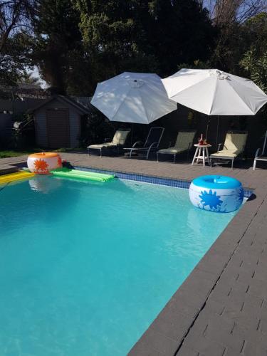 a swimming pool with two umbrellas and chairs and a table at Rekky Signature Guesthouse in Johannesburg