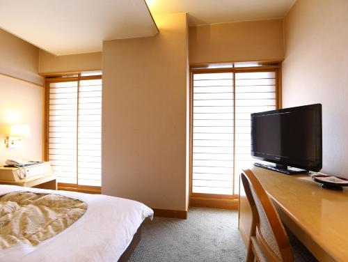 
a bedroom with a bed, tv and window at Kamisuwa Onsen Aburaya Ryokan in Suwa

