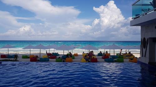 a swimming pool next to a beach with chairs and umbrellas at Cozy and Modern in Cancún
