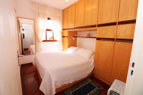 a small bedroom with a white bed and wooden cabinets at Apartamento Vista para as Montanhas in Campos do Jordão