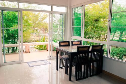 a dining room with a table and chairs and windows at Blue Sky Villa Khao Yai in Pak Chong
