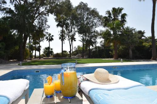 two glasses of orange juice on a table next to a swimming pool at Deluxe First Line Villa in Pervolia