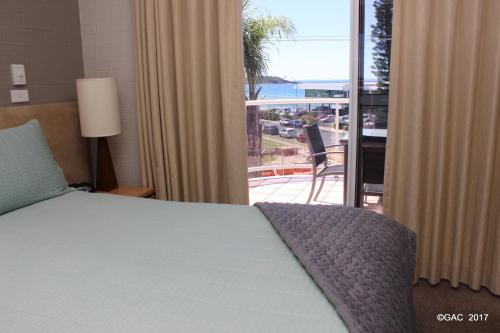 a bedroom with a bed and a view of a balcony at Mollymook Cove Apartments in Mollymook