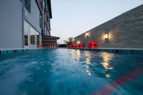 a swimming pool in front of a building with red chairs at Dwella Suvarnabhumi in Lat Krabang