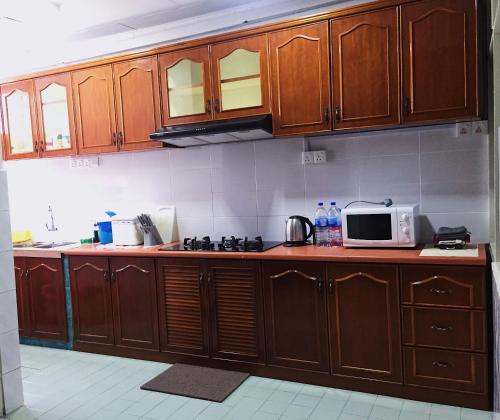 cocina con armarios de madera y microondas en Bayan Baru Homestay @ Taman Sri Nibong en George Town