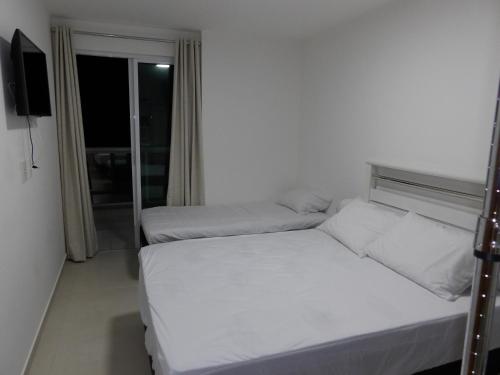 a white bedroom with two beds and a window at Arraial do Cabo in Arraial do Cabo