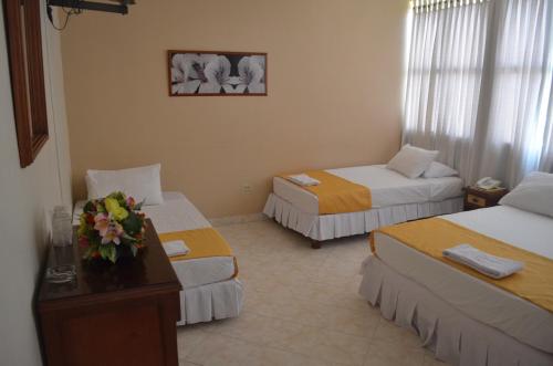 a hotel room with two beds and a table with flowers on it at Hotel El Andino in Cúcuta