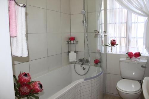 a bathroom with a tub and a toilet and red roses at Plotsklaps Self Catering Cottage in Tokai