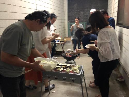 a group of people standing around a grill with food at HappyCloset&WasamonHostel in Kumamoto
