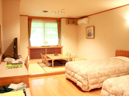a room with two beds and a table and a television at Megahira Onsen Quelle Yoshiwa in Hatsukaichi